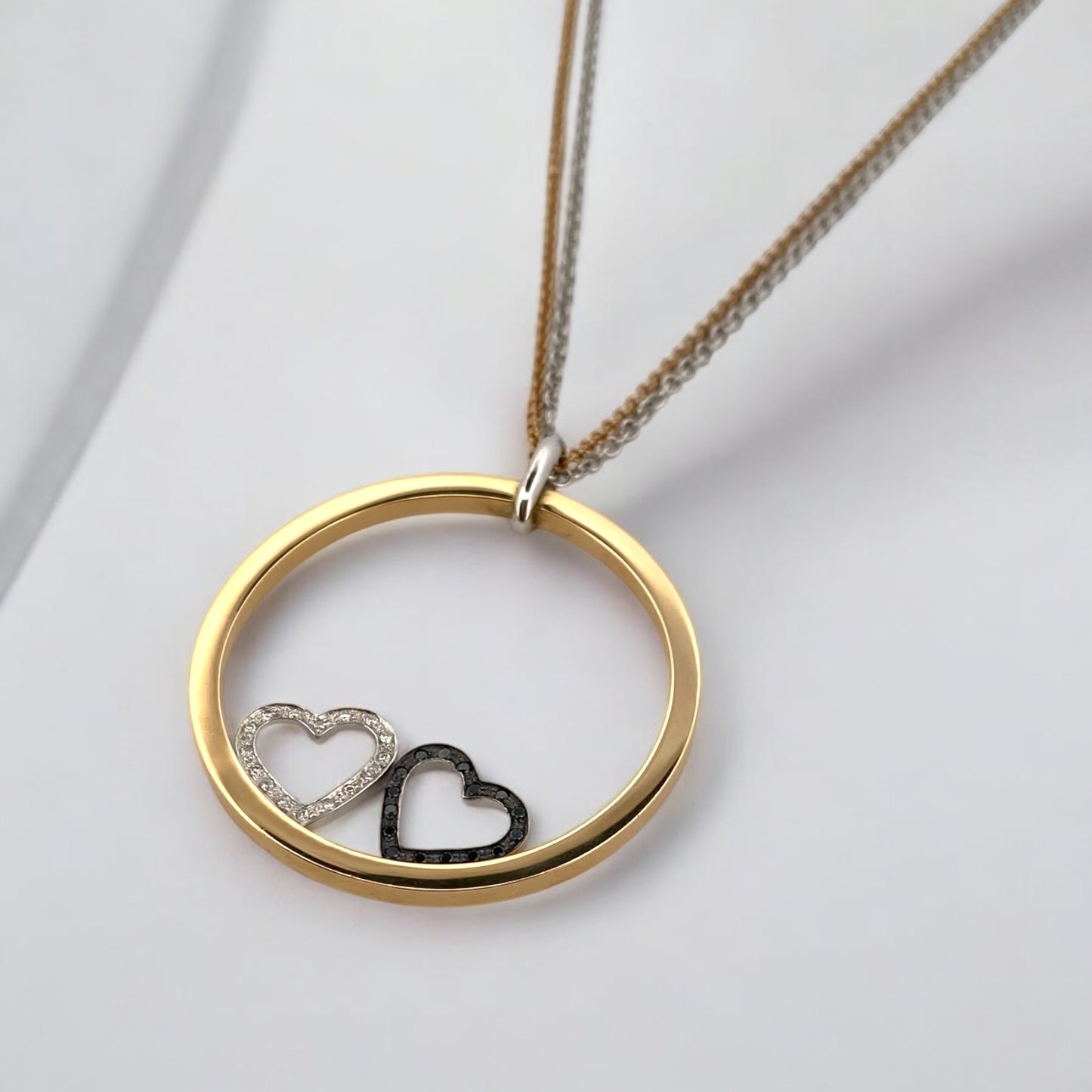 Collar de la firma Pesavento en oro blanco y amarillo de 18kt con circunferencia y dos corazones en su interior. Collar con diamantes negros y blancos.