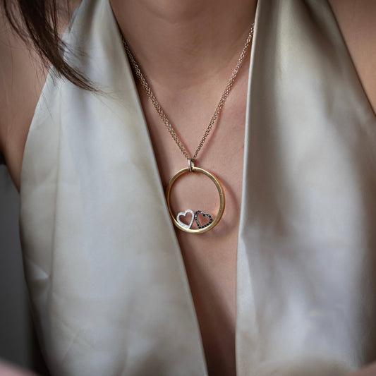 Collar de la firma Pesavento en oro blanco y amarillo de 18kt con circunferencia y dos corazones en su interior. Collar con diamantes negros y blancos.