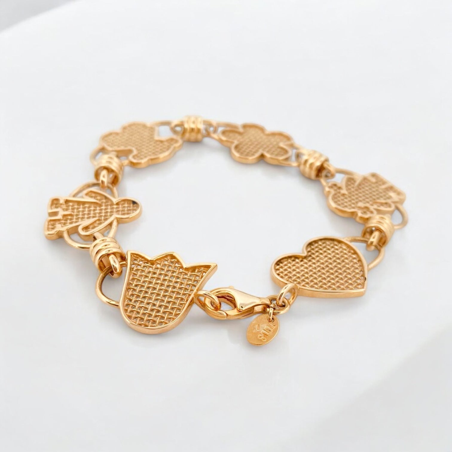 Pulsera original de Tous calada de Oro de 18kt y piezas con motivos de tulipán, osito flor, niña y corazón y cierre tipo mosquetón. La pulsera mide 17,8cm y las piezas 15,86mm. Esta pieza ha sido restaurada en nuestro taller de Barcelona. Compro Oro al mejor precio, joyería segunda mano Barcelona, diseño y transformación de joyas.