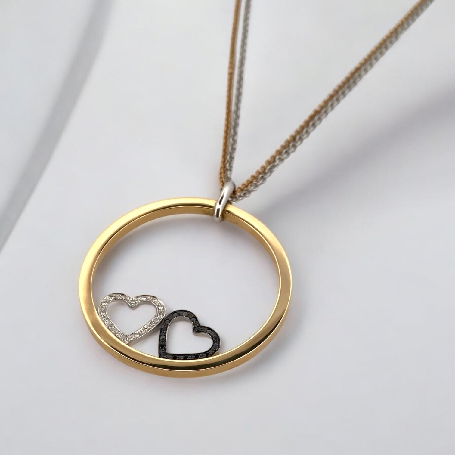 Collar de la firma Pesavento en oro blanco y amarillo de 18kt con circunferencia y dos corazones en su interior. Collar con diamantes negros y blancos.