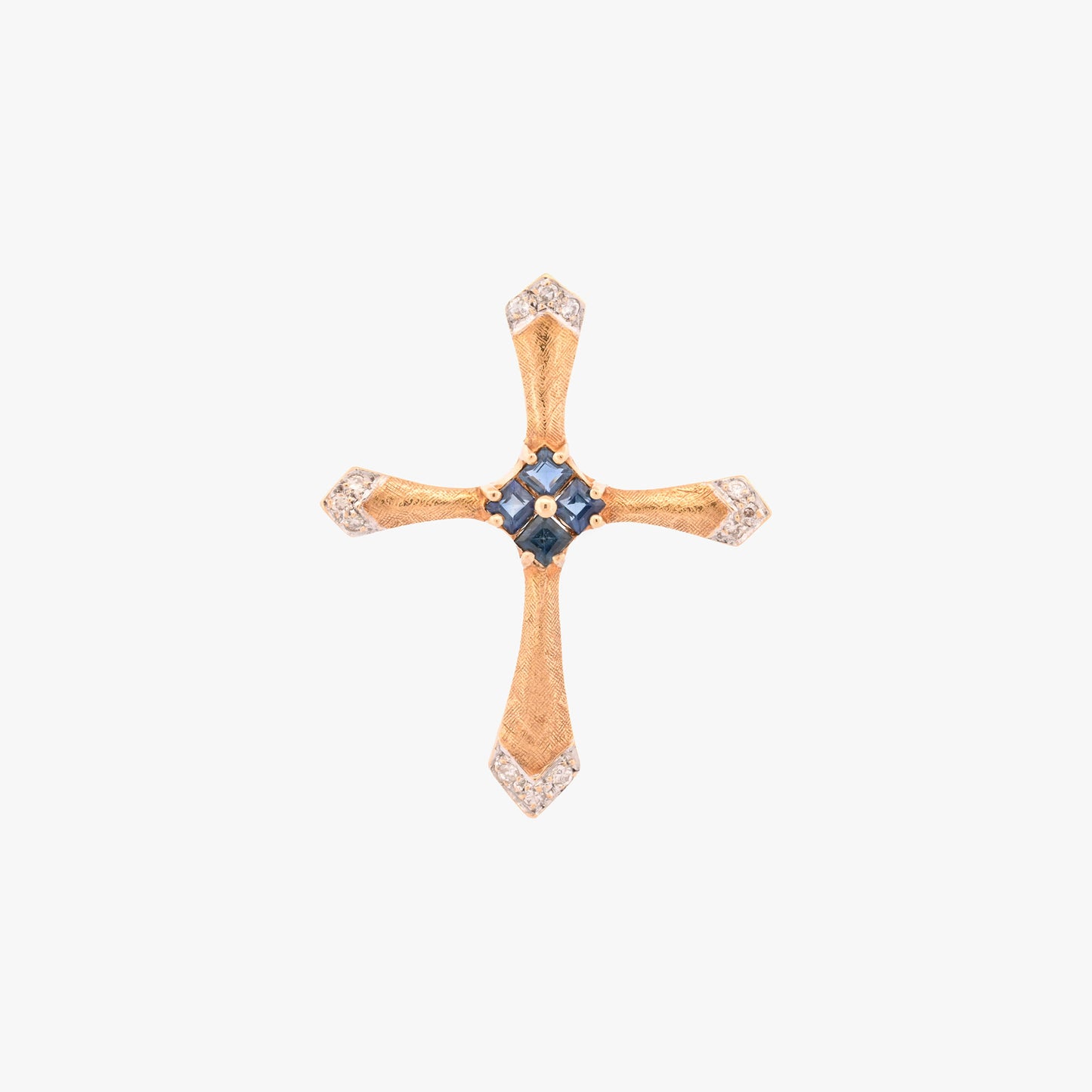 Colgante en forma de cruz latina de oro amarillo de 18kt y combinada con zafiros y brillantes. La cruz destaca por su diseño de líneas curvas estilizadas, un marcado juego de texturas y una cuidada selección de pedreria fina que combina zafiros centrales con pavé de diamantes en los extremos.