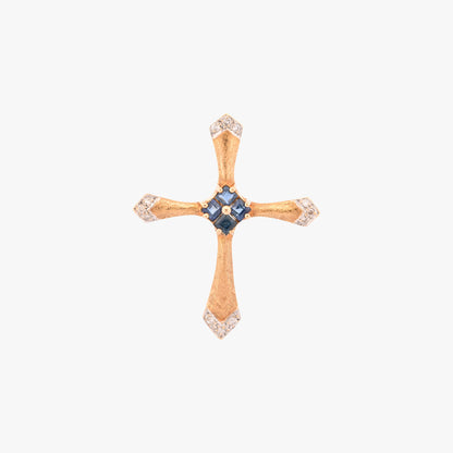 Colgante en forma de cruz latina de oro amarillo de 18kt y combinada con zafiros y brillantes. La cruz destaca por su diseño de líneas curvas estilizadas, un marcado juego de texturas y una cuidada selección de pedreria fina que combina zafiros centrales con pavé de diamantes en los extremos.