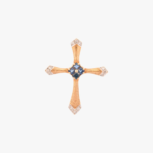 Colgante en forma de cruz latina de oro amarillo de 18kt y combinada con zafiros y brillantes. La cruz destaca por su diseño de líneas curvas estilizadas, un marcado juego de texturas y una cuidada selección de pedreria fina que combina zafiros centrales con pavé de diamantes en los extremos.